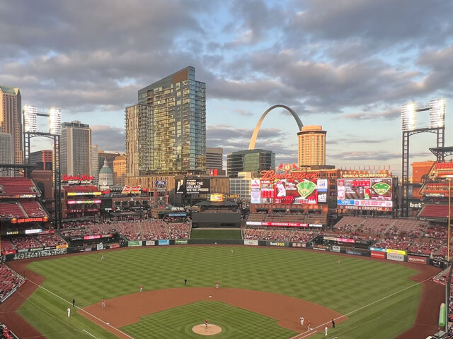 View of the field from behind home plate at Busch Stadium in St. Louis, with the skyline and Gateway Arch in the background