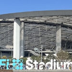 Panoramic view of the exterior of SoFi Stadium in Inglewood, California, with signage in the foreground