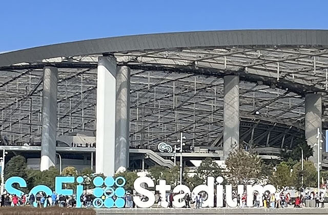 Panoramic view of the exterior of SoFi Stadium in Inglewood, California, with signage in the foreground