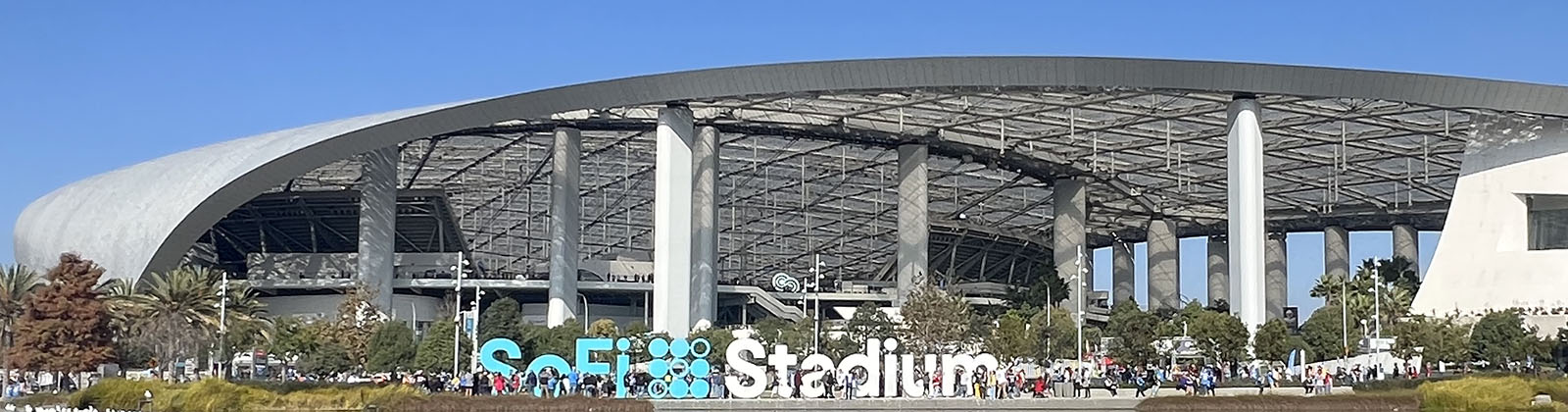 Panoramic view of the exterior of SoFi Stadium in Inglewood, California, with signage in the foreground